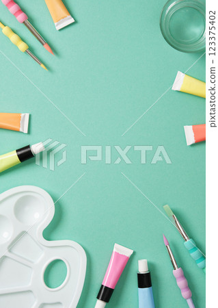 Preparing to painting. Tubes of acrylic paint, brushes, a glass of water on mint green background. Place for your text. 123375402