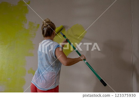 A woman paints an interior wall with a roller brush, displaying her artistic skills A woman paints an interior wall with a roller brush, displaying her artistic skills 123375930