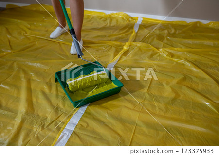 A person painting a room using a roller while standing on a yellow drop cloth for protection A person painting a room using a roller while standing on a yellow drop cloth for protection 123375933