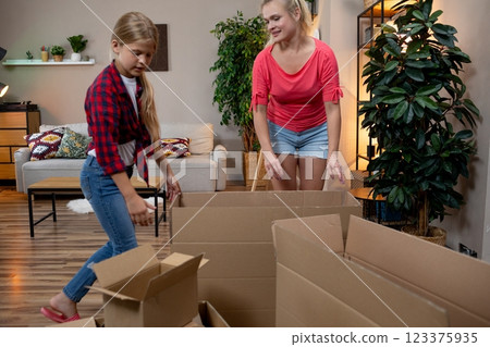 A mother and her daughter are joyfully unpacking boxes together in their new home space 123375935