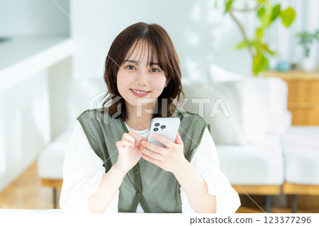 在房間裡操作智慧型手機的年輕女子 在房間裡操作智慧型手機的年輕女子 123377296