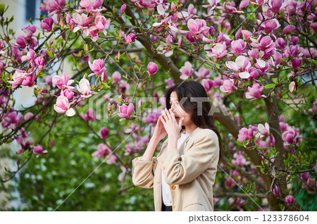 Woman allergic suffering from seasonal allergy at spring in blossoming garden at springtime. Young woman sneezing, having runny nose in front of blooming tree. Spring allergy concept 123378604