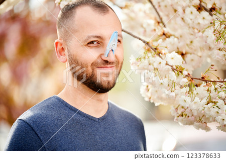 Man allergic suffering from seasonal allergy at spring. Bearded man with clothespin clipped to his nose - symbolic gesture of his inability to breathe due to nasal congestion near blooming tree. Man allergic suffering from seasonal allergy at spring. Bearded man with clothespin clipped to his nose - symbolic gesture of his inability to breathe due to nasal congestion near blooming tree. 123378633