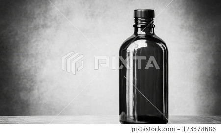 Dark glass bottle standing alone on a textured surface in shadows 123378686