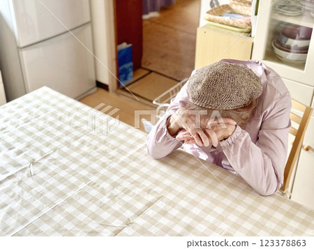 Elderly woman with her hands on her forehead at the kitchen table, drooping, facing left 123378863