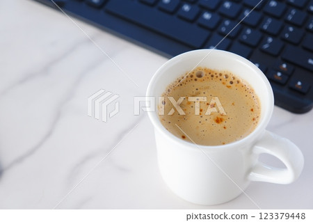 An image of someone working at a desk on a laptop while drinking a freshly brewed delicious cafe latte 123379448