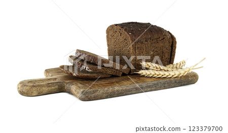 A rustic wooden board displays a loaf of dark bread, freshly sliced, next to golden wheat stalks 123379700