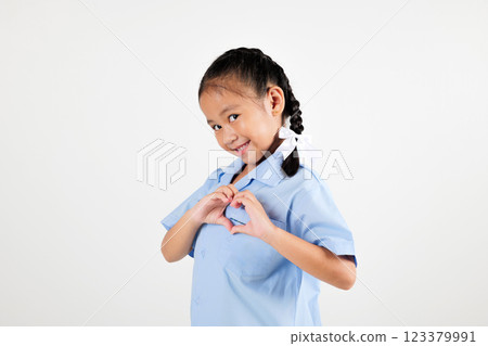 Portrait smile Asian little girl kindergarten holding hands together on chest in heart shape studio isolated white background, happy woman kid wear school uniform showing heart gesture, back to school 123379991