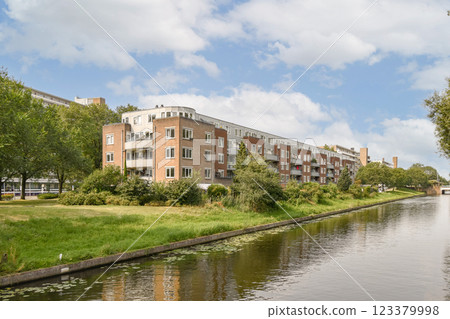 A serene view of a river lined with modern residential buildings and lush greenery under a blue sky. Ideal for showcasing urban life and nature. A serene view of a river lined with modern residential buildings and lush greenery under a blue sky. Ideal for showcasing urban life and nature. 123379998