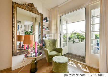 A beautifully designed interior featuring a green armchair and a decorative mirror, opening to a refreshing balcony filled with plants. 123380009