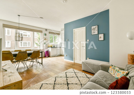 A stylish living room featuring a blue accent wall, comfortable seating, and ample natural light, creating an inviting atmosphere for relaxation and socializing. 123380033