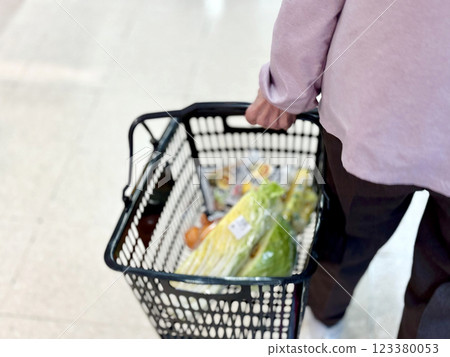An elderly woman walking with vegetables in her shopping basket 123380053