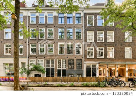A view of elegant buildings blending historic architecture with modern design, featuring large windows amidst vibrant greenery and a lively street scene. 123380054