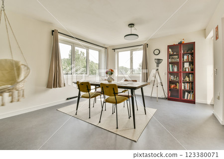 A contemporary dining area featuring a stylish table, chairs, and natural light pouring in through large windows. Minimalistic decor enhances its elegance. 123380071