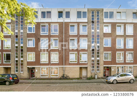 A contemporary apartment building showcasing a blend of brick and glass architecture. Featuring multiple windows for natural light and an urban street view. 123380076