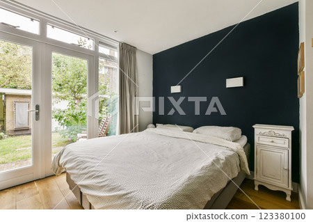 A stylish bedroom featuring contemporary design, large windows, and a view of a garden. Soft textures and muted colors create a serene atmosphere. A stylish bedroom featuring contemporary design, large windows, and a view of a garden. Soft textures and muted colors create a serene atmosphere. 123380100