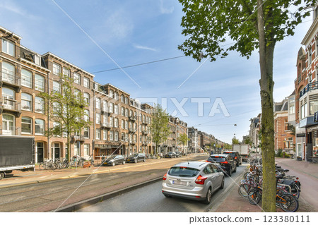 A picturesque urban scene showcasing a tree-lined street with parked cars and historic buildings, ideal for city exploration or architectural appreciation. 123380111