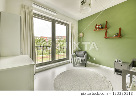 A stylish nursery featuring a green accent wall, a cozy armchair, and large windows offering plenty of natural light, creating a serene atmosphere for a child's room. A stylish nursery featuring a green accent wall, a cozy armchair, and large windows offering plenty of natural light, creating a serene atmosphere for a child's room. 123380118