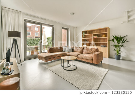A contemporary living room showcasing a cozy sofa, a stylish coffee table, and indoor plants, creating a welcoming atmosphere. Natural light fills the space through large windows. 123380130