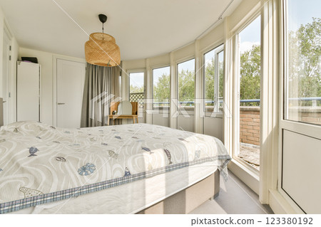 A beautifully designed modern bedroom featuring large windows that provide ample natural light, a comfortable bed, and a minimalistic decor style, perfect for relaxation. 123380192