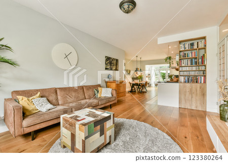 A stylish living room featuring a comfortable sofa, wooden flooring, and an open dining space with natural light streaming in. Perfect for modern home aesthetics. 123380264