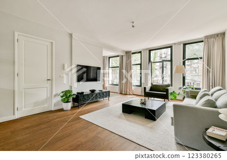 A stylish and modern living room featuring large windows, a comfortable sofa, and elegant decor elements, creating a warm and inviting atmosphere. 123380265