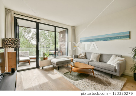 A stylish modern living room featuring a neutral sofa, natural light through large windows, and cozy decor elements that create a welcoming atmosphere. 123380279