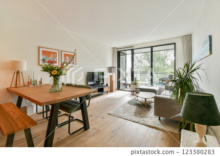A bright and modern living space featuring a cozy seating area, elegant decor, and large windows that invite natural light and greenery indoors. 123380283