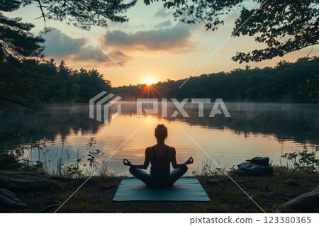 A woman meditating in the morning sun by the lake 123380365