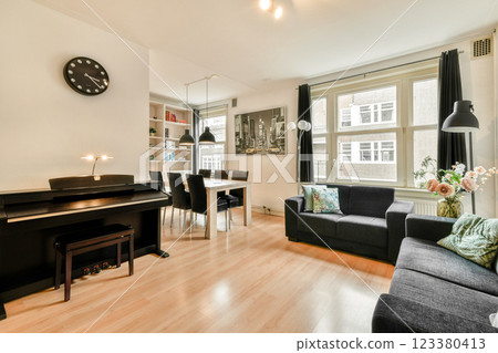 A stylish, modern living room featuring a piano, comfortable seating, and well-lit space with large windows. Perfect for relaxation and social gatherings. 123380413