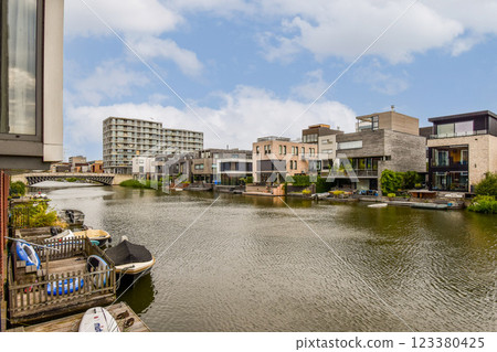 Stylish modern homes line a serene riverbank, showcasing contemporary architecture amidst lush greenery and blue skies. 123380425
