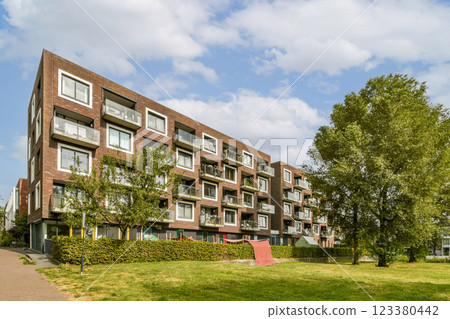 A contemporary residential structure with multiple balconies nestled among lush greenery under a blue sky. The scene combines urban living with nature. 123380442