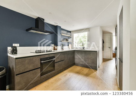 A sleek modern kitchen featuring a minimalist design with dark blue walls, stylish cabinets, and natural lighting from a window. 123380456