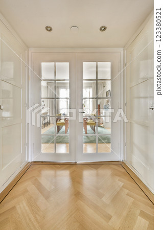 A stylish entrance featuring elegant double glass doors, leading into a bright and contemporary living space with a warm wooden floor. 123380521