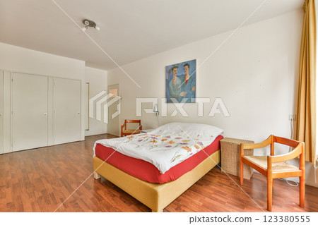 A bright and spacious bedroom featuring a comfortable bed with decorative bedding. Natural light fills the room, enhancing the minimalist decor. 123380555