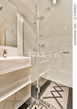 This contemporary bathroom features a sleek design with a glass shower, minimalistic sink, and stylish floor rug, creating a clean and elegant atmosphere. 123380663