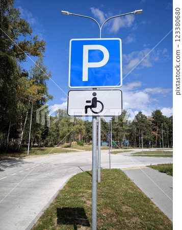 The sign "Parking for the disabled only" on the background of street trees. It allows permit holders to park in an area reserved only for drivers or passengers with disabilities. 123380680