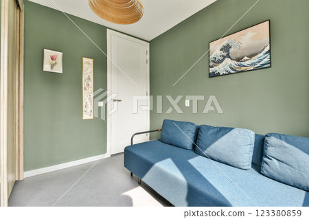 A contemporary interior space featuring a comfortable blue sofa and decorative wall art against soothing green walls, creating a tranquil environment. A contemporary interior space featuring a comfortable blue sofa and decorative wall art against soothing green walls, creating a tranquil environment. 123380859
