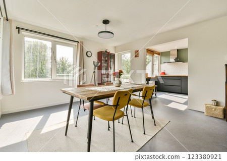 A stylish dining area featuring a wooden table, chairs, and large windows allowing ample daylight, creating a cozy and inviting atmosphere. 123380921