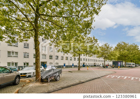 A vibrant urban street scene showcasing modern architecture, lush green trees, and parked cars along a circular road in a city environment. 123380961