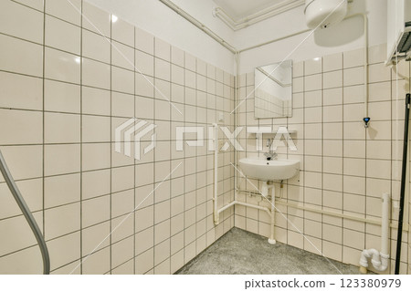 A minimalist bathroom featuring tiled walls, a small sink, and a mirror. The design emphasizes functionality and cleanliness with neutral colors. A minimalist bathroom featuring tiled walls, a small sink, and a mirror. The design emphasizes functionality and cleanliness with neutral colors. 123380979