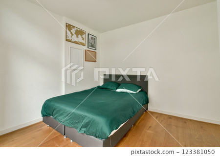 A serene and minimalist bedroom featuring a green bedspread, wooden flooring, and simple wall decor that creates a relaxing atmosphere for rest. A serene and minimalist bedroom featuring a green bedspread, wooden flooring, and simple wall decor that creates a relaxing atmosphere for rest. 123381050