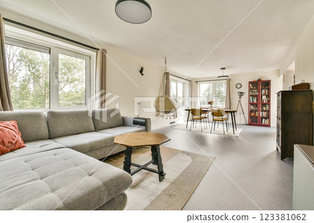 A stylish and inviting living room featuring a comfortable sofa, wooden furniture, and large windows allowing natural light to fill the space. A stylish and inviting living room featuring a comfortable sofa, wooden furniture, and large windows allowing natural light to fill the space. 123381062