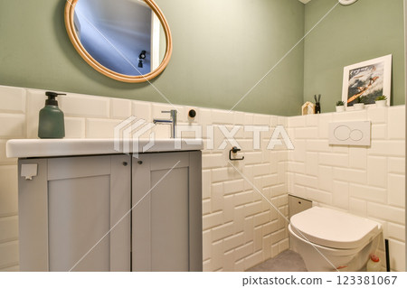 Elegant bathroom featuring a minimalist design with a round mirror, soft green walls, and stylish fixtures, creating a serene space for relaxation. 123381067