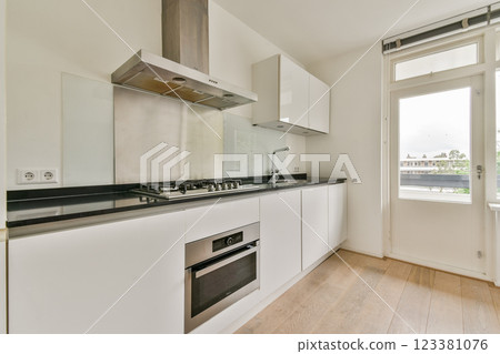 A sleek modern kitchen featuring stainless steel appliances, white cabinetry, and an open window allowing natural light. The minimalist design emphasizes functionality. 123381076