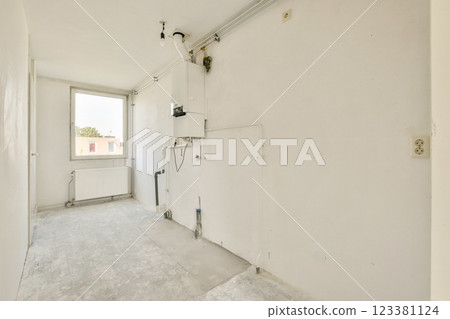 A minimalistic, empty room featuring white walls and an unadorned floor. Natural light filters in through a window, emphasizing the simplicity of the space. 123381124