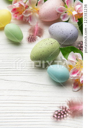 Colorful easter eggs and spring flowers creating festive border on white wood Colorful easter eggs and spring flowers creating festive border on white wood 123381236