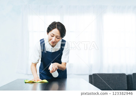 A middle-aged woman wearing an apron cleaning a room 123382946