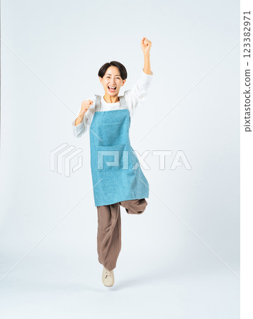 Full-body photo of a middle-aged woman wearing an apron jumping Full-body photo of a middle-aged woman wearing an apron jumping 123382971