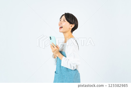 一名身穿圍裙的中年婦女帶著微笑使用智慧型手機 123382985